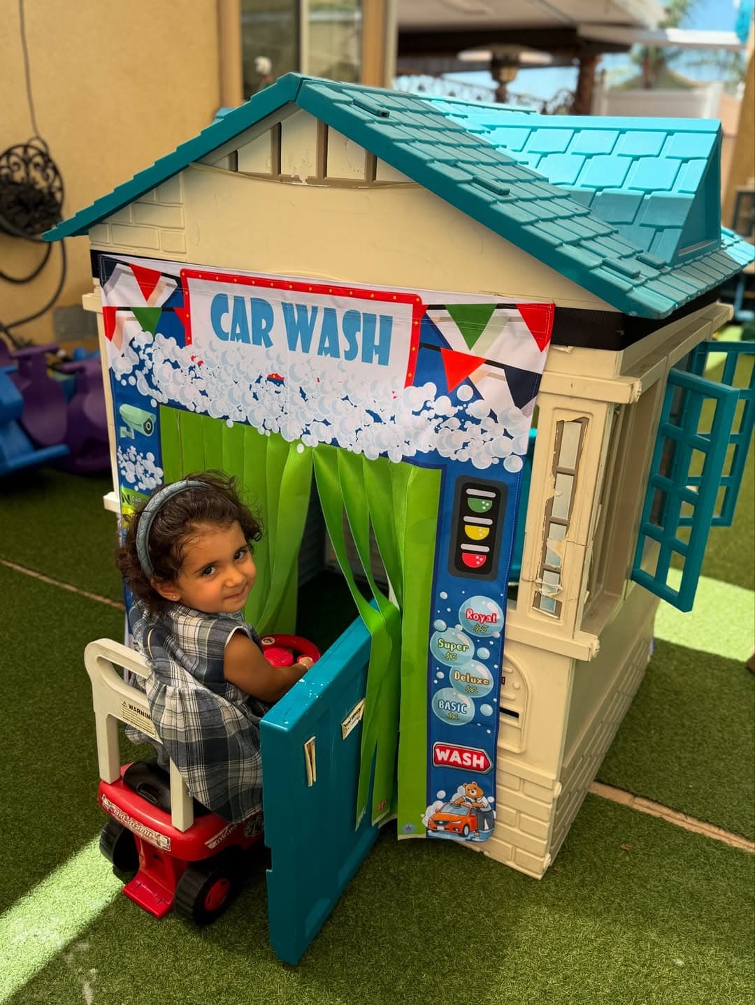Child peeking out from inside the Car Wash playhouse on a ride-on car