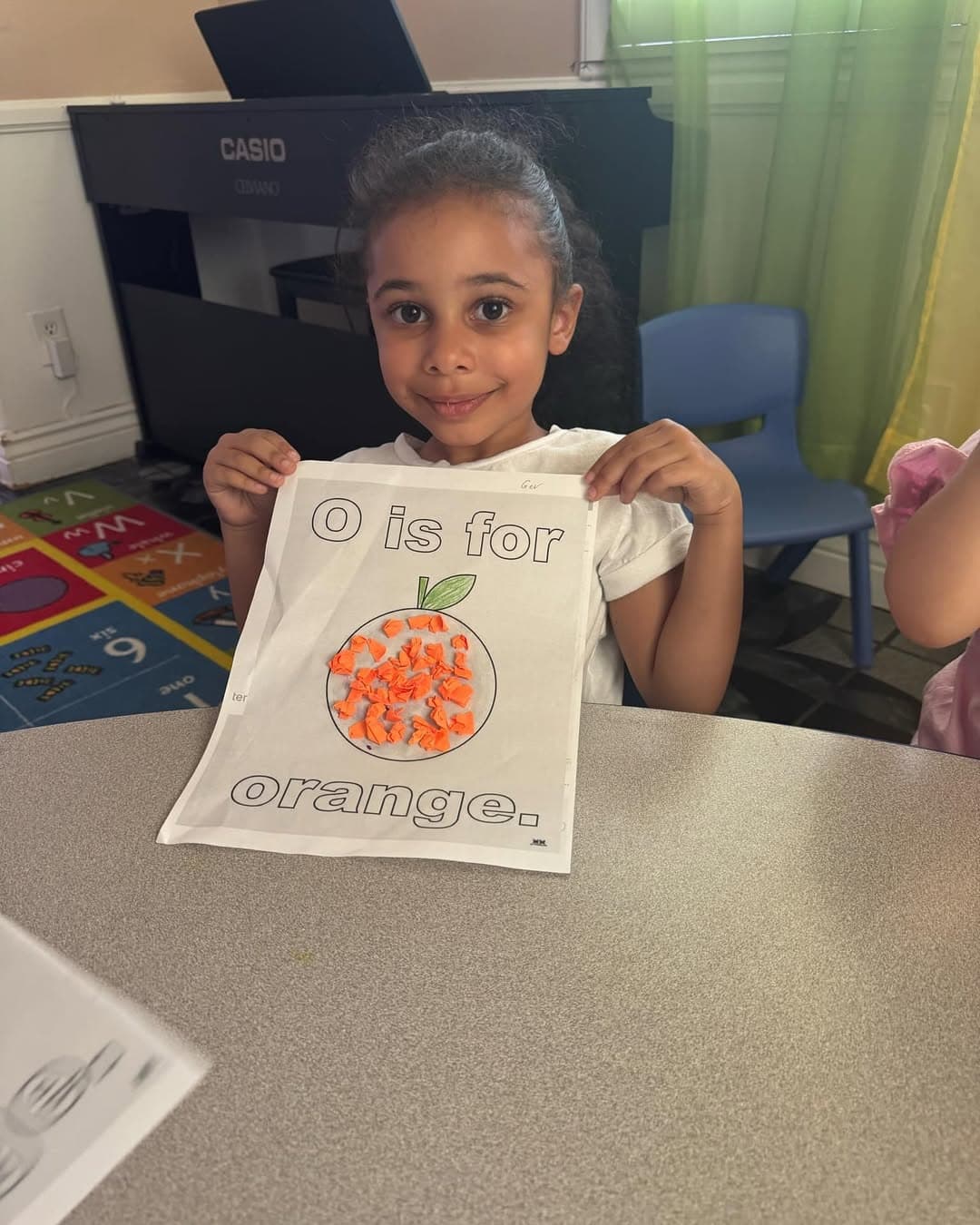 Child proudly holding up an 'O is for orange' paper craft