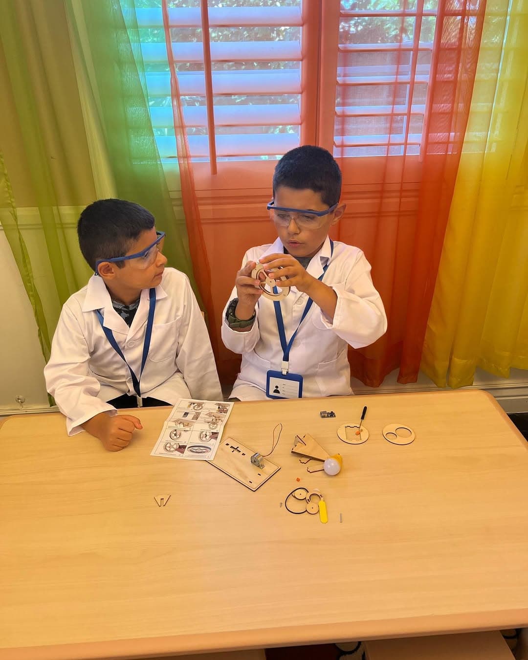 Two children in lab coats and safety goggles building a science kit