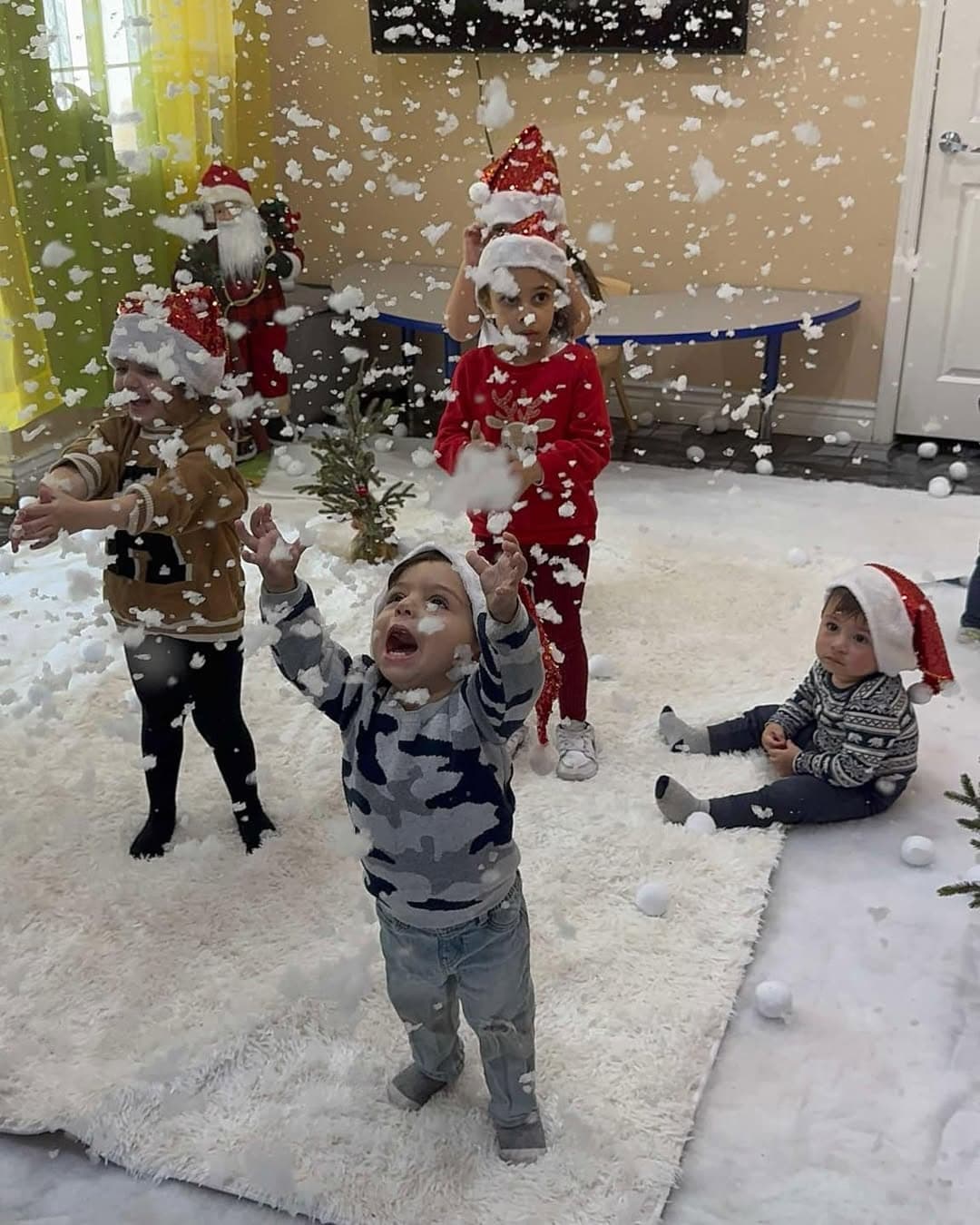 Children wearing Santa hats playing in falling indoor snow